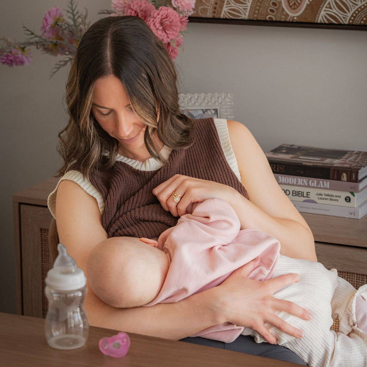 A mum breastfeeding her baby with a Minbie bottle nearby
