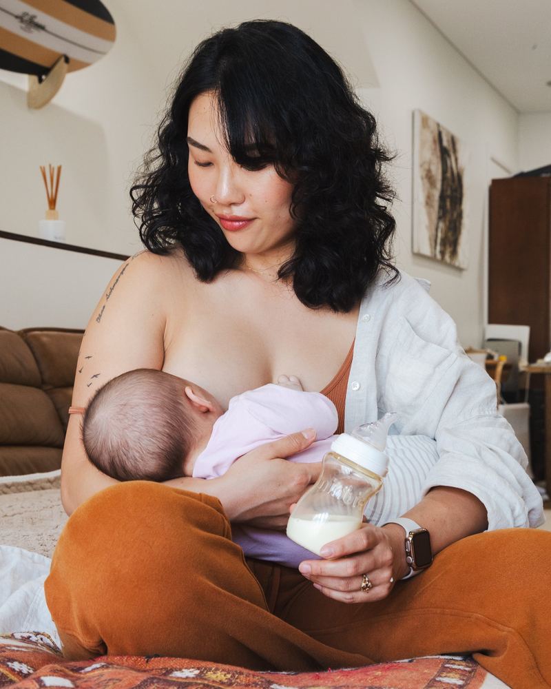 A mum breastfeeding while holding a Minbie bottle